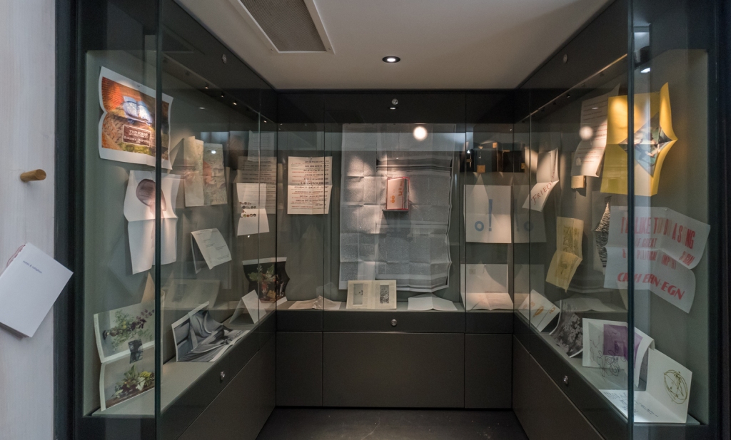 A glass display case filled with printed sheets which make up the folded pages of the book.